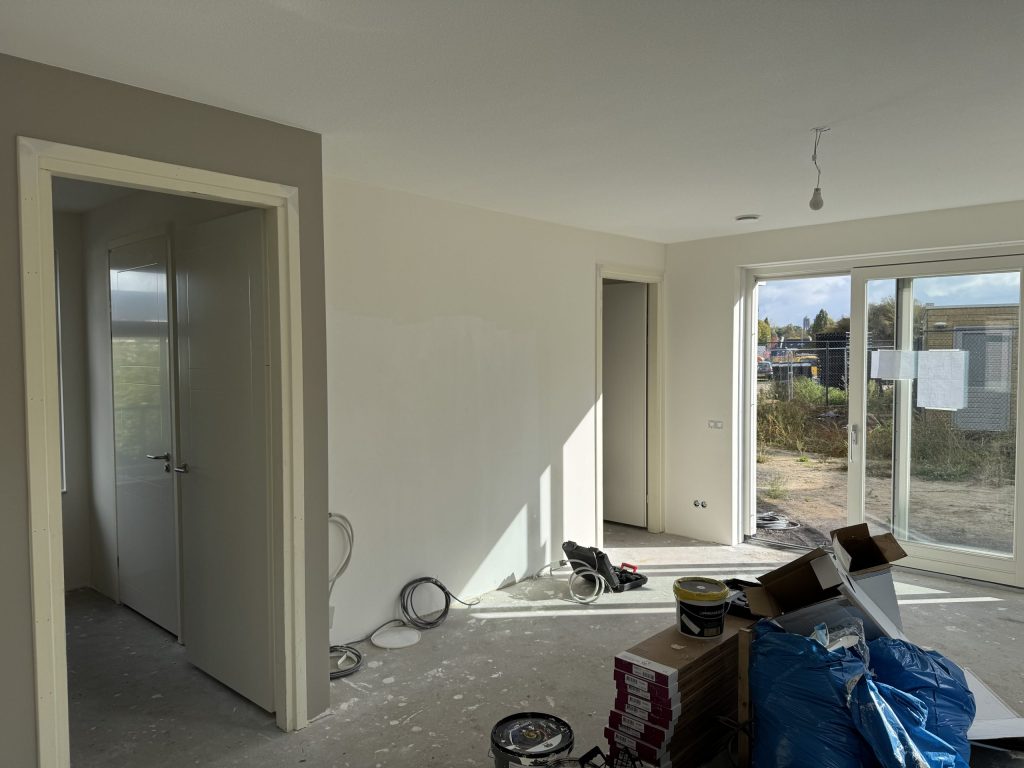 Nieuwbouwwoonkamer tijdens de afwerking, met verfemmers en materiaal op de betonvloer