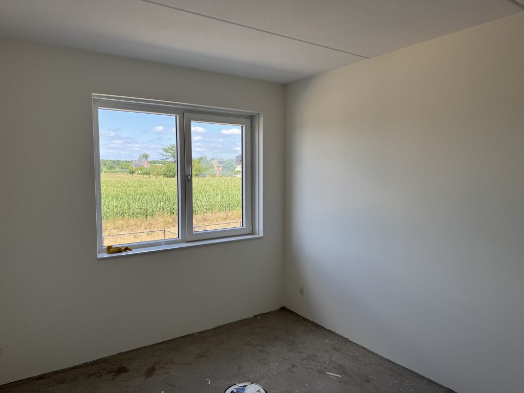 Lege nieuwbouwkamer met gladde, lichte wanden en een raam met uitzicht op het land